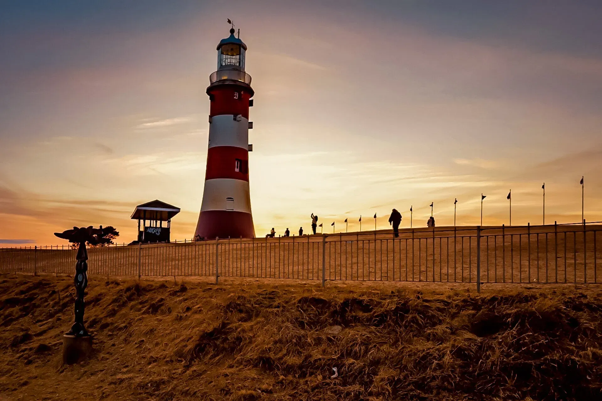 A lighthouse and visitors silhouetted against the setting sun
